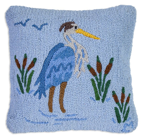 Blue hooked wool pillow featuring a Great Blue Heron standing in a pond surrounded by cattails. 