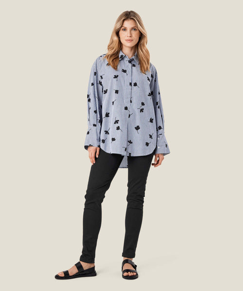 Masai Gila Tunic in maritime blue pattern. blue and white stripes with blue leaf silhouetted scattered throughout. Button up, long sleeves with flared cuffs, oversized fit.