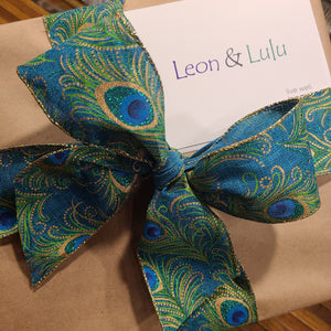 Fancy blue and green bow with peacock moifs and Leon & Lulu's logo on a white card.