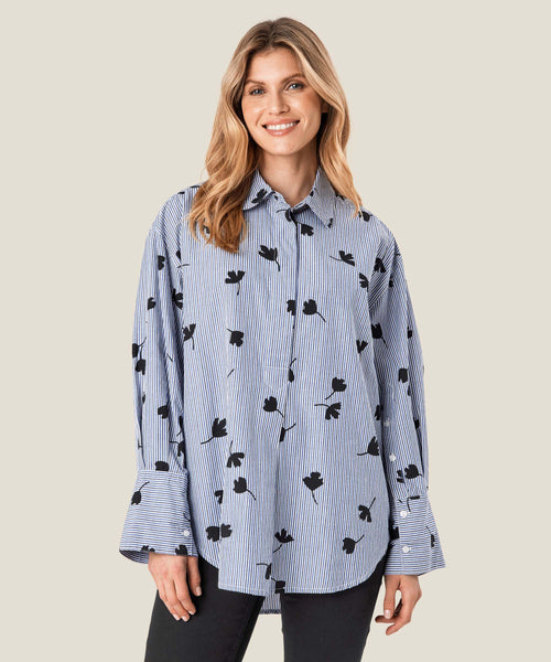 Masai Gila Tunic in maritime blue pattern. blue and white stripes with blue leaf silhouetted scattered throughout. Button up, long sleeves with flared cuffs, oversized fit.