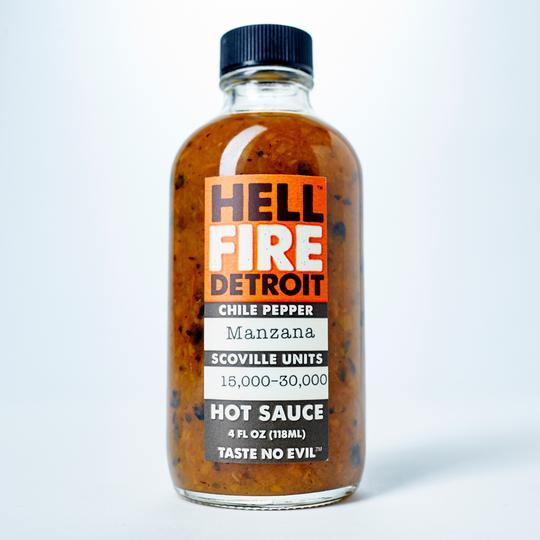 4 fluid ounce glass bottle with a black twist off cap filled with hot sauce. Has orange, black, and white label with text, "Hell Fire Detroit, Chile Peppers, Manzana, Scoville Units 15,000 - 30,000 Hot Sauce. "