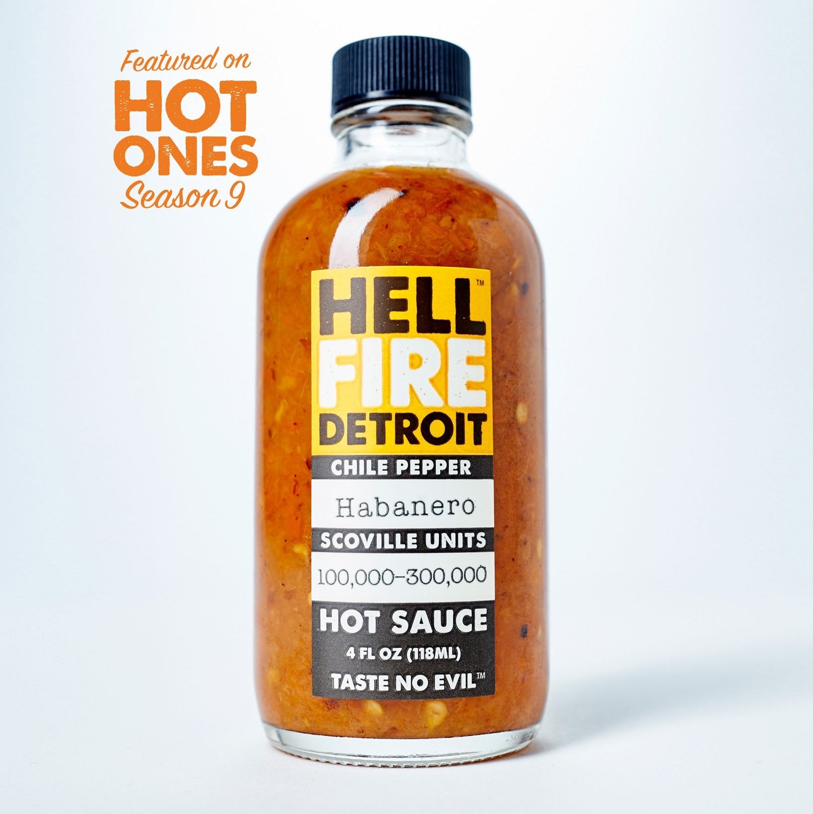 4 fluid ounce glass bottle with a black twist off cap filled with hot sauce. Has yellow, black, and white label with text, "Hell Fire Detroit, Chile Peppers, Habanero, Scoville Units 100,000 - 300,000 Hot Sauce. "
