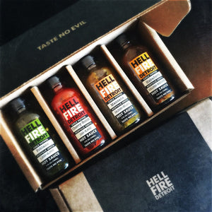 Black cardboard box with the text, "Taste no evil." Contains 4 bottles of different colored hot sauces of various levels of spiciness.